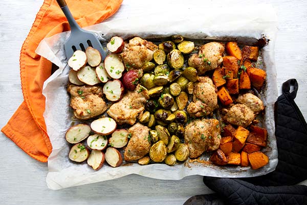Overhead view of Chicken and Veggies Sheet Pan Dinner with a spatula and orange napkin