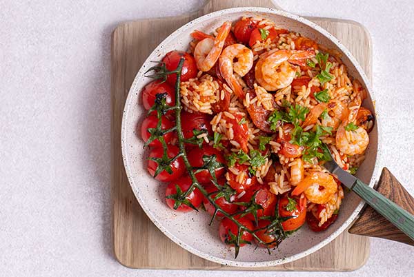 Chorizo and Shrimp Paella in a white skillet on top of a wooden cutting board