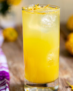 Citrus & Marigold Cocktail with citrus zest on top on a wooden table with bright purple and white napkin on the side