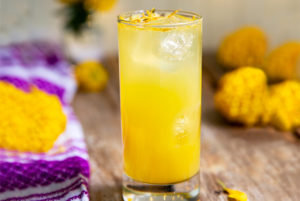 Citrus & Marigold Cocktail with citrus zest on top on a wooden table with bright purple and white napkin on the side