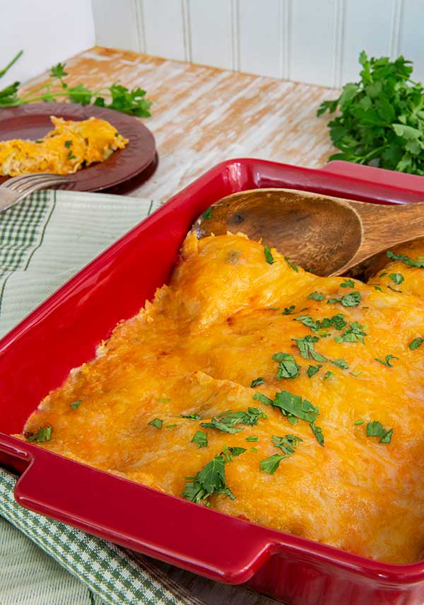 Easy Green Chile Enchiladas in a red rectangular baking dish topped with cilantro