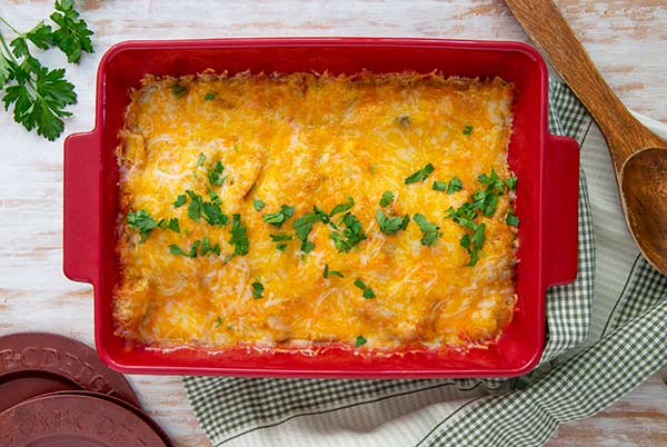 Overhead view of Easy Green Chile Enchiladas in a red baking dish on light wood background