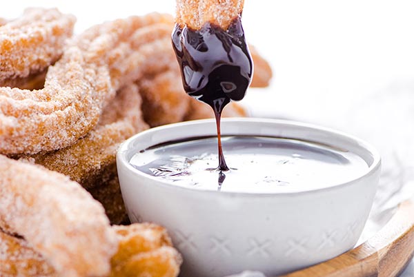 Closeup of Gluten-Free Churros with one churro being dipped in chocolate sauce