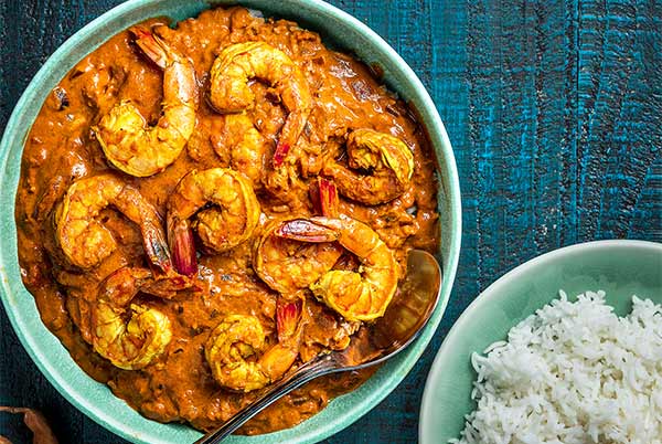 Goan Shrimp in a light teal bowl with a bowl of white rice on the side on a dark teal background