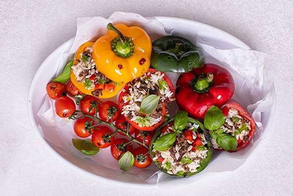 Greek Stuffed Bell Peppers with a wine of roasted tomatoes next to them on a white oval platter