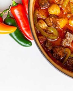 Hungarian Goulash in a pot with fresh peppers next to it on a white background