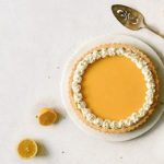 Overhead view of a gluten-free Lemon Tart on a white plate with lemons around it on a white background