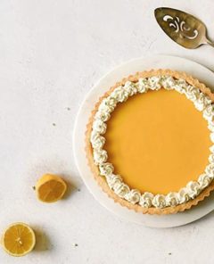 Overhead view of a gluten-free Lemon Tart on a white plate with lemons around it on a white background