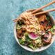 Overhead view of Maple Curry Garlic Ramen Noodle Bowl with wooden chopsticks on a light blue background