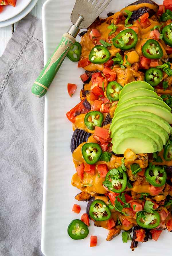 Overhead view of Nacho Momma's Roasted Vegetables Recipe topped with avocado and jalapenos on a white rectangular platter