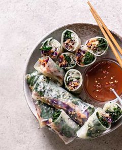 Sesame Kale Spring Rolls in a white and beige bowl with sauce on the side and wooden chopsticks