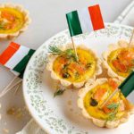smoked salmon tartlets with dill and capers with mini Irish flags in them on a white plate with green decoration