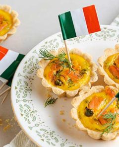 smoked salmon tartlets with dill and capers with mini Irish flags in them on a white plate with green decoration