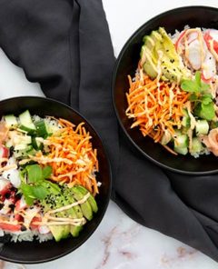 Overhead view of two California Sushi Bowls in black bowls with a black cloth napkin set between the bowls