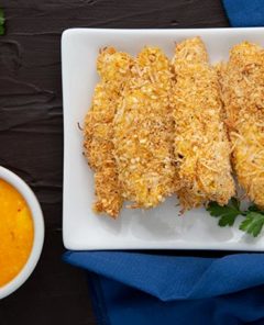 Overhead view of Coconut Chicken Tenders with Mango Chutney on a white rectangular plate on a dark background with navy blue napkin