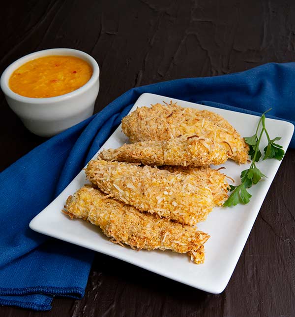 Coconut Chicken Tenders with Mango Chutney on a white rectangular plate on dark background with navy blue napkin