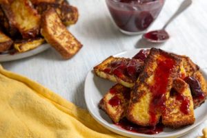 Overhead view of white plates with French Toast Sticks with Cherry Sauce and a yellow cloth napkin on the side