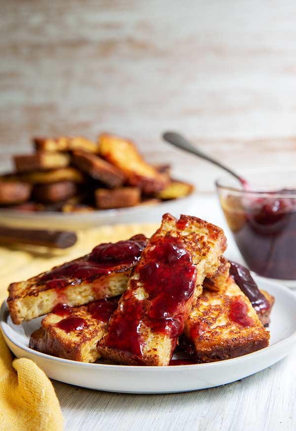 French Toast Sticks with Cherry Sauce on a white plate on a light white and beige background with a bowl of cherry sauce in the background