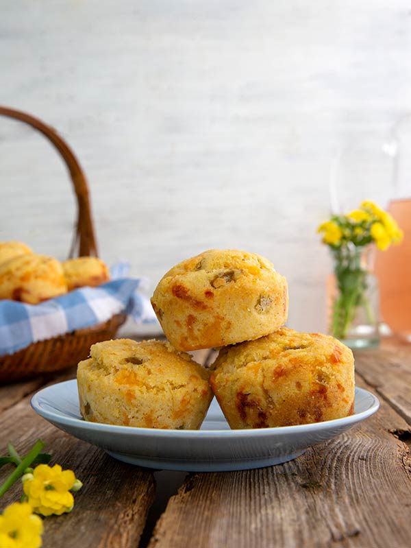 Green Chile Corn Muffins Recipe stacked on a plate with a picnic basket in the background with more muffins in it