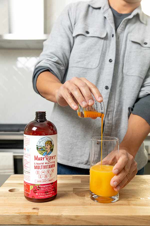 Man pouring MaryRuths Liquid Multi Vitamin into a glass of orange juice