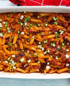 Overhead view of Plant-Based Chili Sin Carne Pasta Bake in a white baking dish with red kitchen towel underneath on a pale blue background