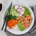 Overhead view of Salmon Poke Bowls in a white bowl with black chopsticks and a gray napkin