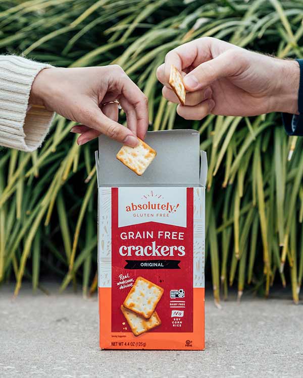 Two hands pulling crackers out of an Absolutely GF Crackers box