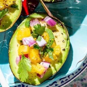 Closeup of Avocado Pineapple Salsa Boats on a teal plate with colorful plate and tablecloth underneath