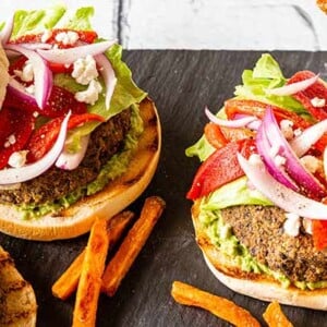 Black Rice Veggie Burgers on a slate board with a bowl of sweet potato fries on the side