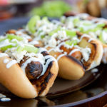Closeup of Buffalo style hot dogs topped with blue cheese and celery on a black plate