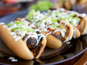 Closeup of Buffalo style hot dogs topped with blue cheese and celery on a black plate