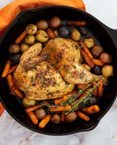 Overhead view of Cast-Iron Roasted Half Chicken Recipe on a white marble counter with orange napkin under the skillet