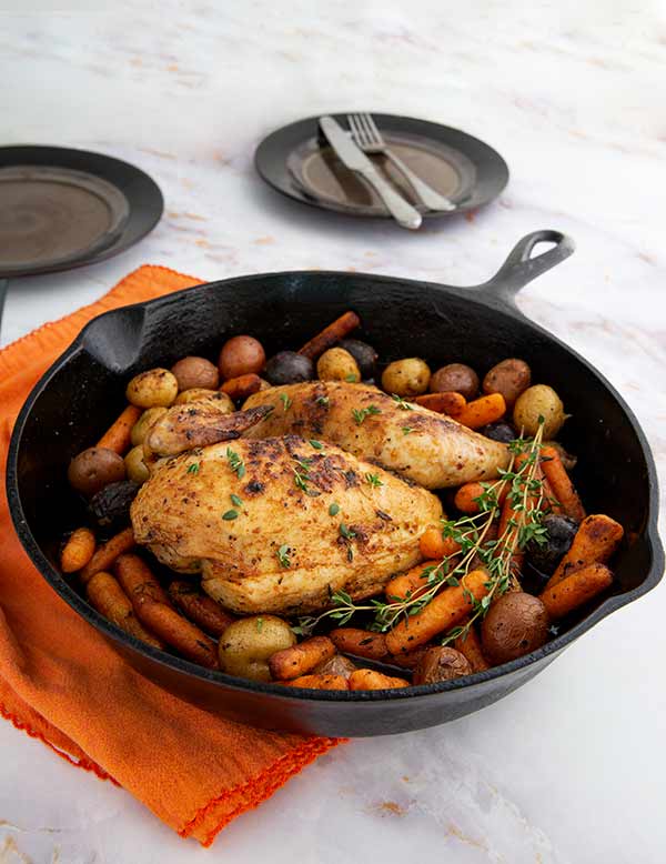Cast-Iron Roasted Half Chicken Recipe on a white marble counter with orange napkin under the skillet