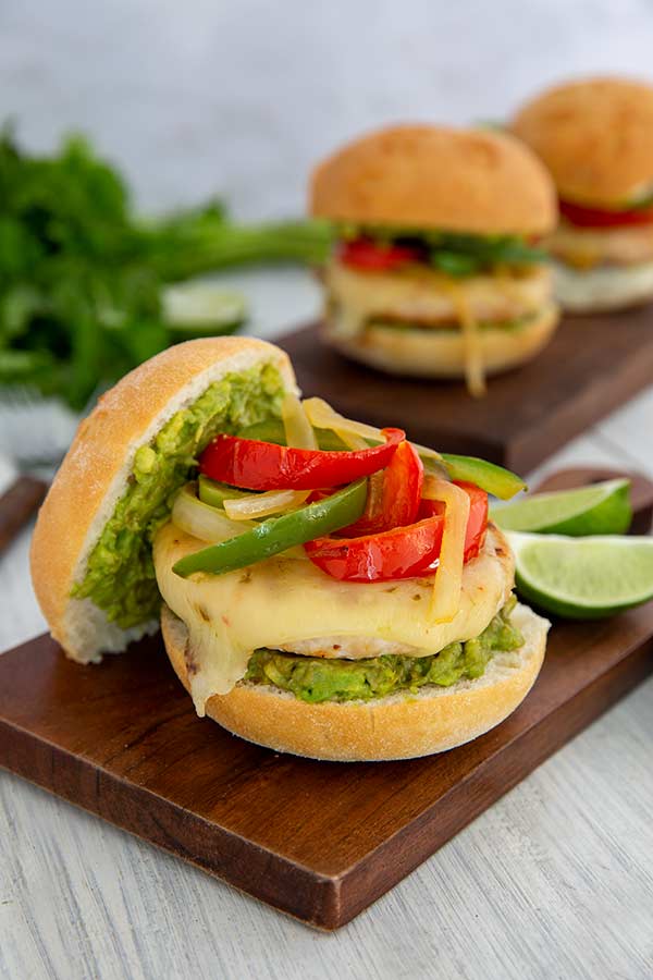 Chicken Fajita Burgers on wooden planks on a white-washed wood table with cilantro and limes in the background