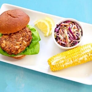 Overhead view of Crab Cakes with Corn on the Cob and coleslaw on a rectangular white platter on a bright blue background
