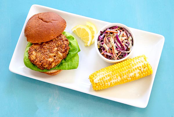 Overhead view of Crab Cakes with Corn on the Cob and coleslaw on a rectangular white platter on a bright blue background