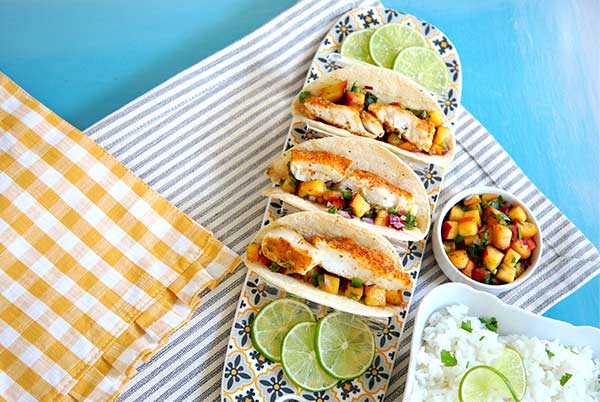 Overhead view of Fish Tacos on a blue and yellow floral platter on a blue background with white rice and salsa on the side