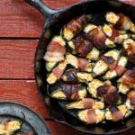 Overhead view of Grilled Jalapeno Peppers wrapped in bacon in a cast iron skillet on a reddish brown table