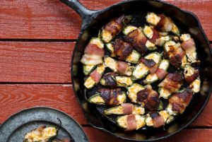Overhead view of Grilled Jalapeno Peppers wrapped in bacon in a cast iron skillet on a reddish brown table