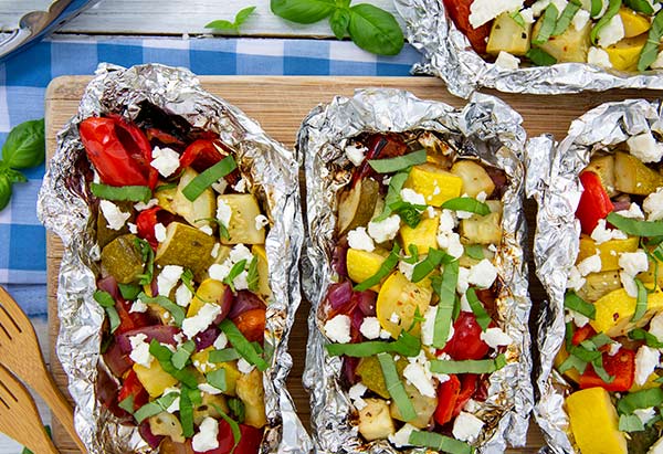 Overhead view of Grilled Veggie Packets in tin foil on a wood cutting board with light blue and white napkin underneath