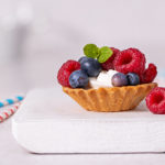 Closeup of Mini Berry Tarts topped with raspberries and blueberries and fresh mint on a white board