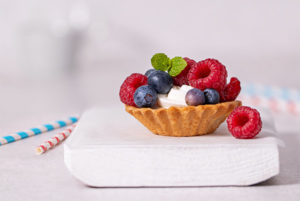 Closeup of Mini Berry Tarts topped with raspberries and blueberries and fresh mint on a white board
