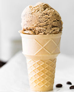 No-Churn Coffee Ice Cream in an ice cream code with coffee beans next to it on parchment paper with a white background