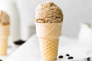 No-Churn Coffee Ice Cream in an ice cream code with coffee beans next to it on parchment paper with a white background