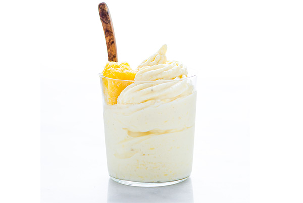 Pineapple Whip in a glass topped with pineapple chunks with a wooden spoon isolated on a white background