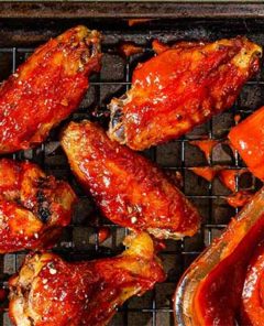 Overhead view of Sticky Mango Chicken Wings on a wire rack on a baking sheet with glass bowl of sauce and sauce brush