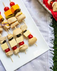 Bagel Skewers with bagels and cheese and tomato on a white platter on top of a white linen picnic blanket on a grass field