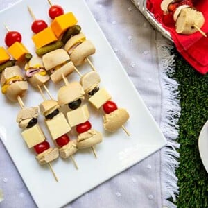 Bagel Skewers with bagels and cheese and tomato on a white platter on top of a white linen picnic blanket on a grass field