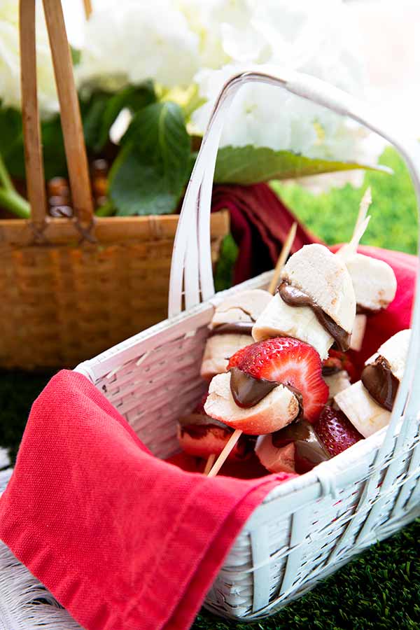 Bagel Skewers with bagen pieces and strawberries in a picnic basket with red cloth napkin inside