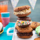 Stack of Easy Ice Cream Sandwiches on a white tray on a teal placemat with bright cups and punch and a party banner in the background